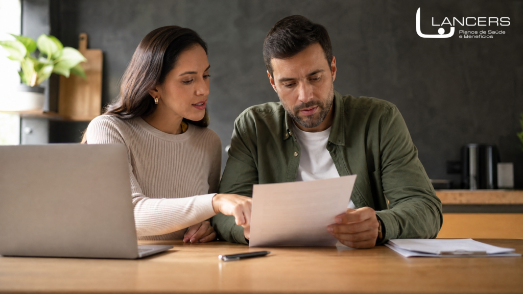 Casal analisando contrato de plano de saúde com carência em laptop e documentos na mesa da cozinha